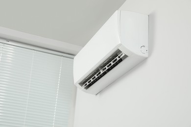 Modern air conditioner on white wall indoors, low angle view