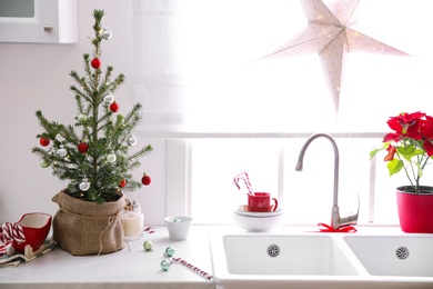 Small Christmas tree decorated with baubles and festive lights in kitchen