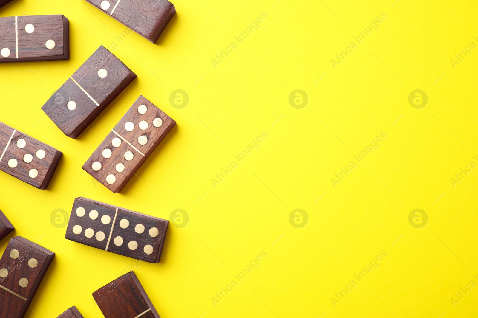 Photo of Wooden domino tiles on yellow background, flat lay. Space for text