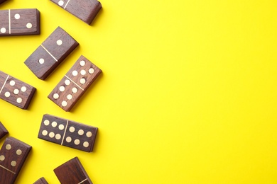 Photo of Wooden domino tiles on yellow background, flat lay. Space for text