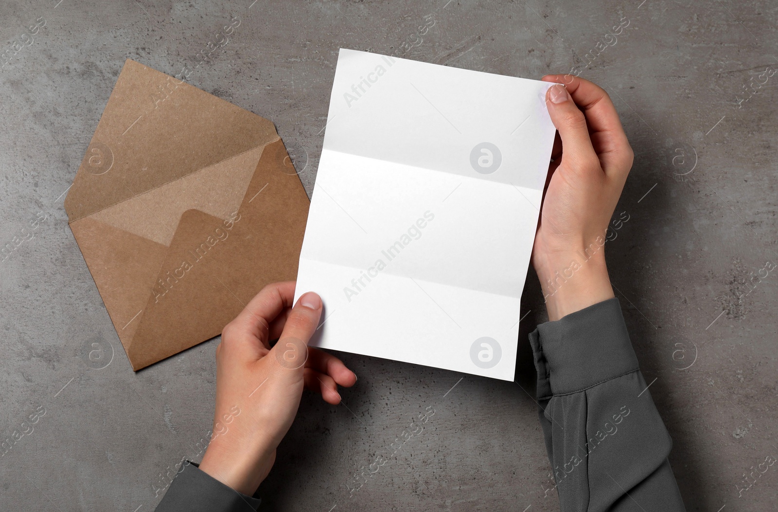 Photo of Woman with blank sheet of paper at grey textured table, top view. Space for text