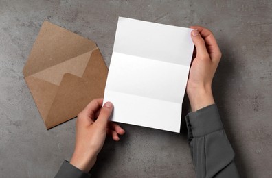 Woman with blank sheet of paper at grey textured table, top view. Space for text