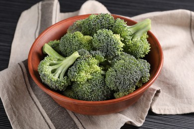 Photo of Bowl with fresh raw broccoli on black wooden table