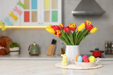 Photo of Easter decorations. Bouquet of tulips, painted eggs and bunny figure on table indoors. Space for text