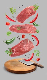 Beef meat and different spices falling on grey background