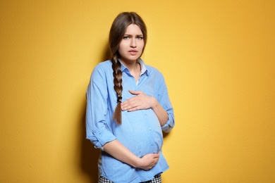 Photo of Young pregnant woman suffering from headache on color background
