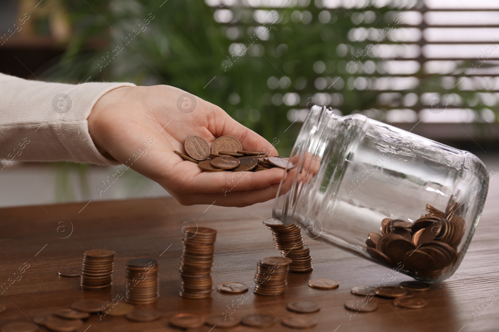 Photo of Woman putting coins into glass jar at wooden table indoors, closeup