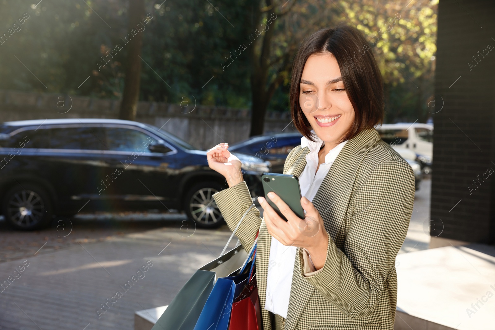 Photo of Special Promotion. Happy young woman with shopping bags and smartphone on city street