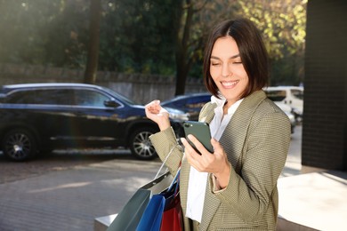 Special Promotion. Happy young woman with shopping bags and smartphone on city street