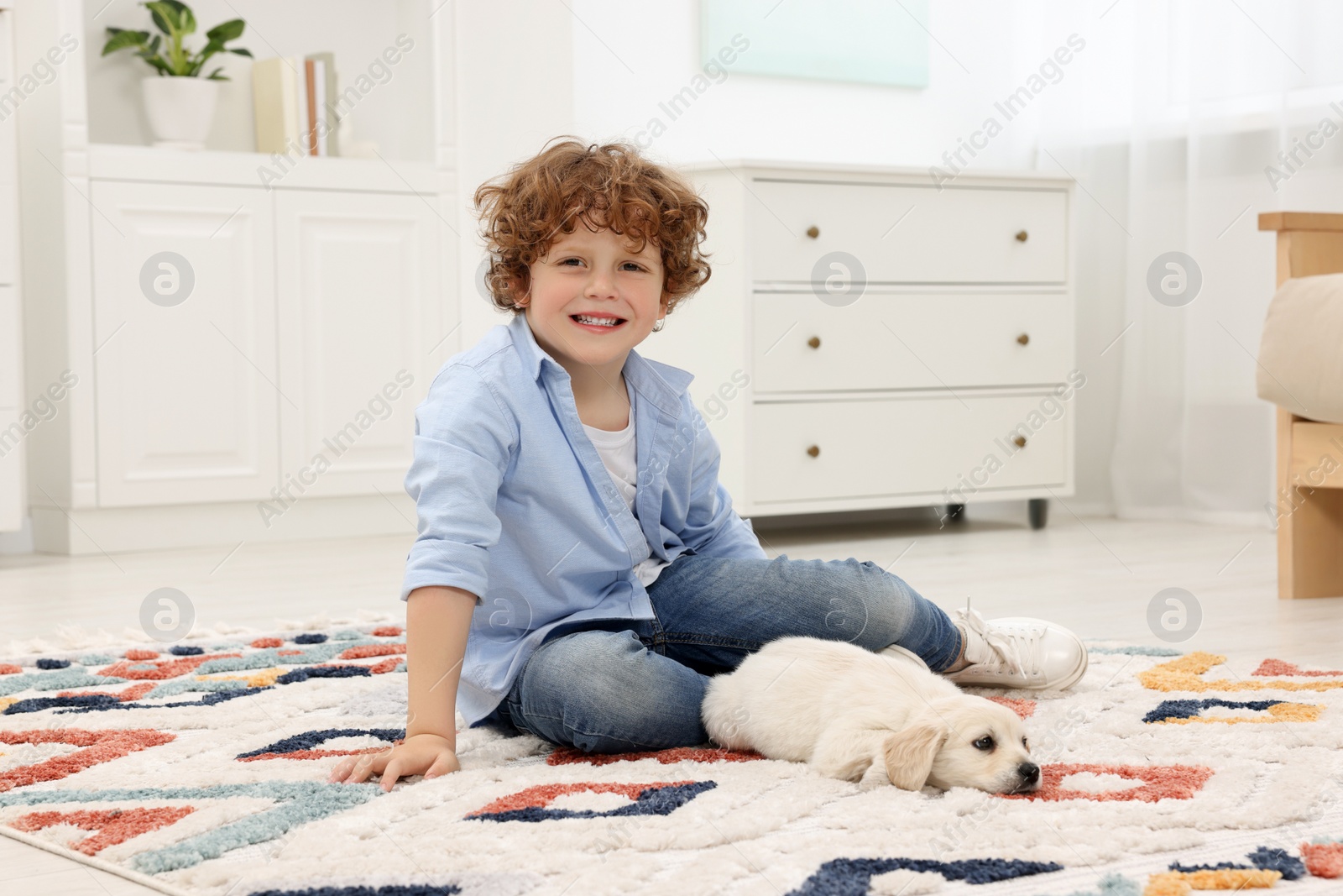 Photo of Little boy with cute puppy on carpet at home