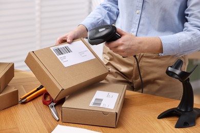 Photo of Parcel packing. Post office worker with scanner reading barcode at wooden table indoors, closeup