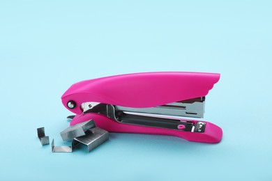 Photo of New bright stapler with staples on light blue background. School stationery