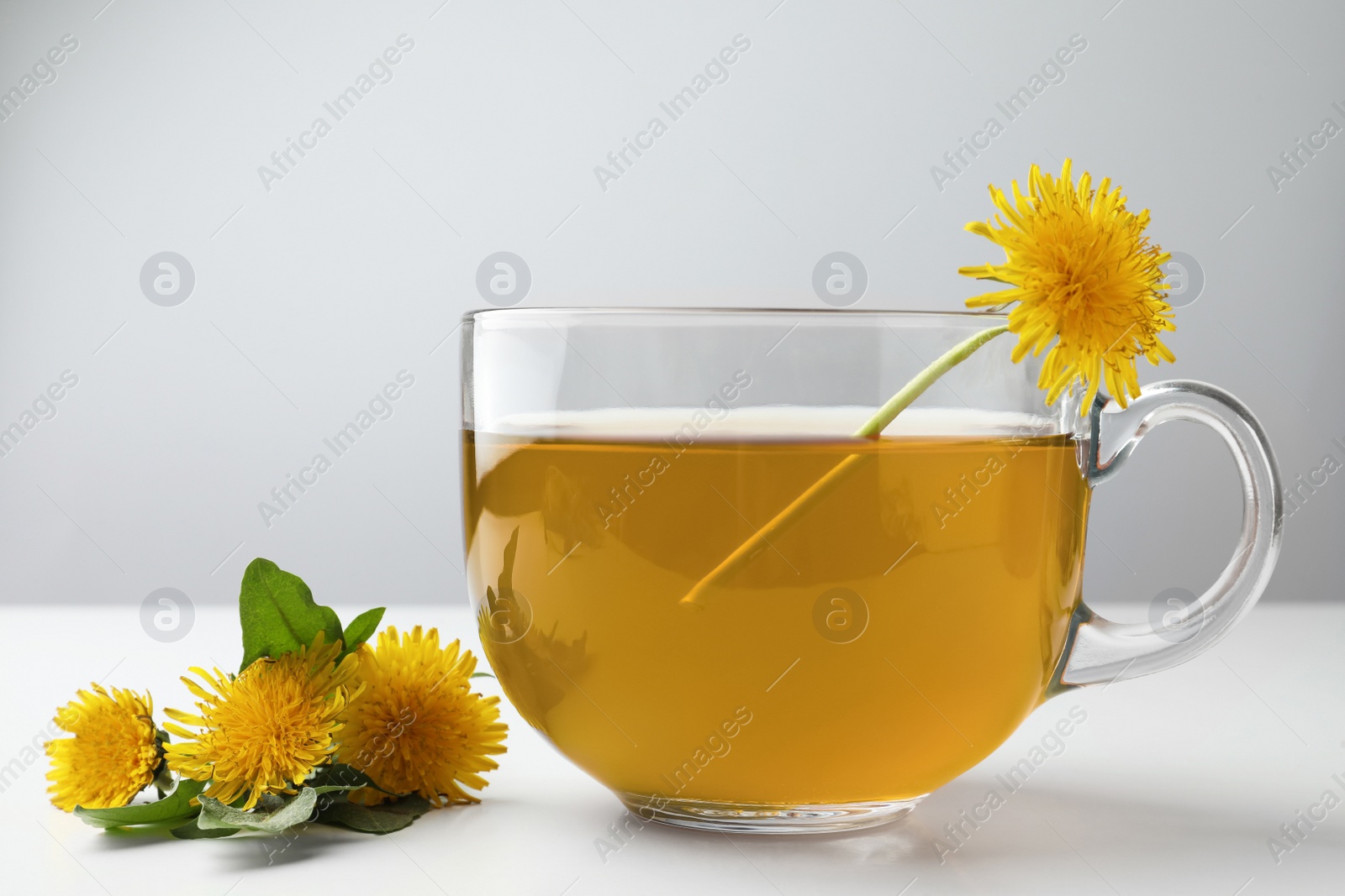 Photo of Delicious fresh tea and beautiful dandelion flowers on white table