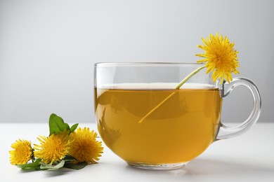 Delicious fresh tea and beautiful dandelion flowers on white table