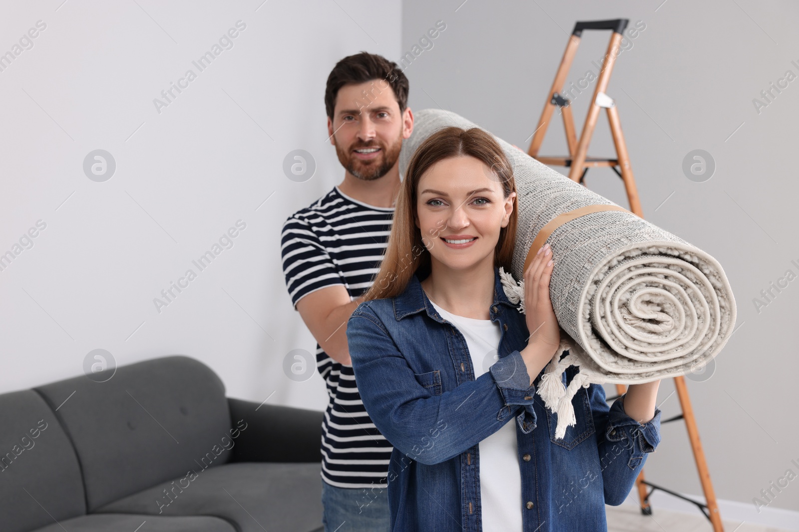 Photo of Smiling couple holding rolled carpet in room