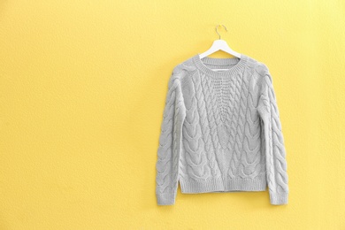 Hanger with stylish sweater on yellow wall. Space for text