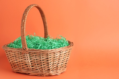 Photo of Easter basket with green paper filler on coral background, space for text