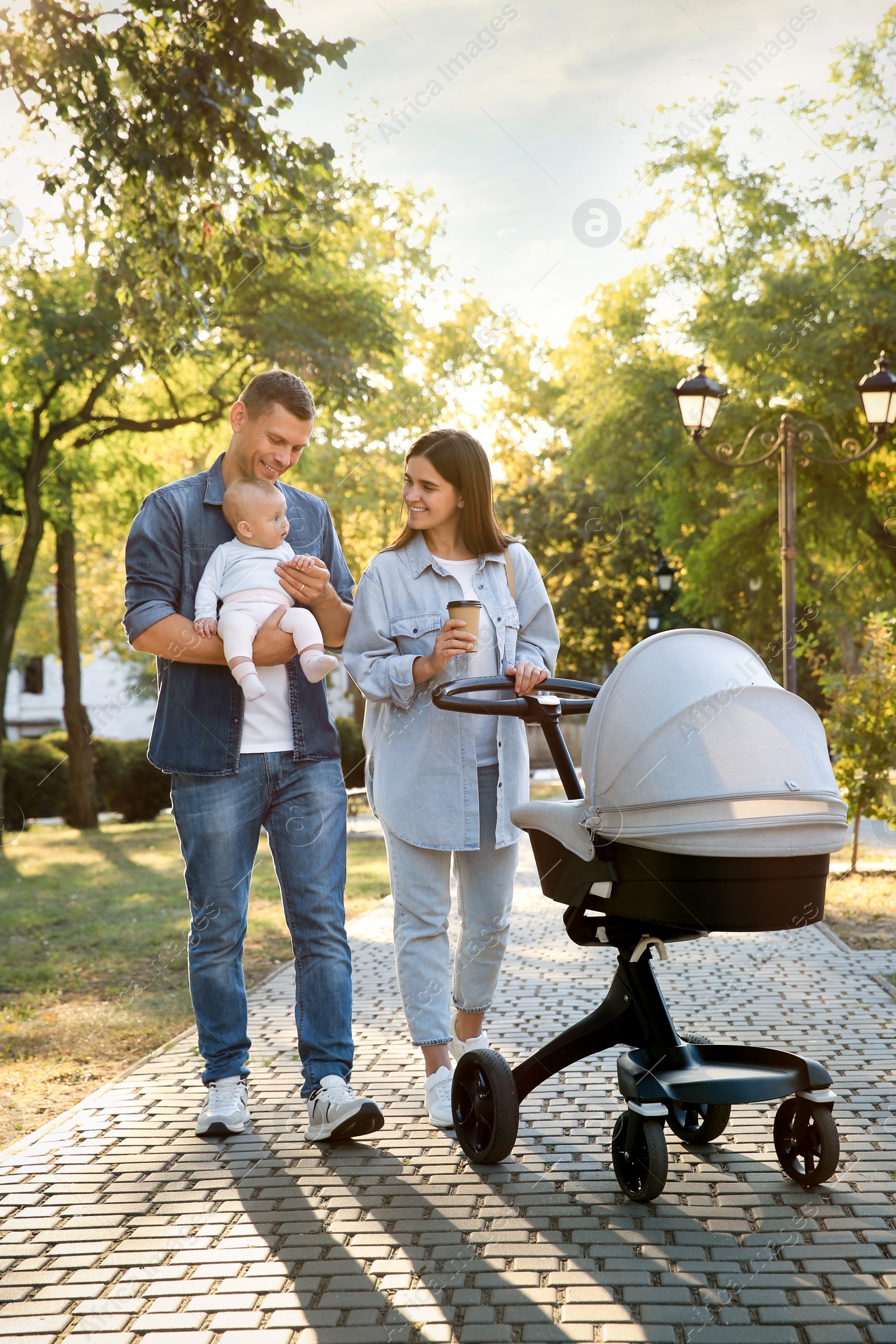 Photo of Happy parents walking with their baby in park on sunny day