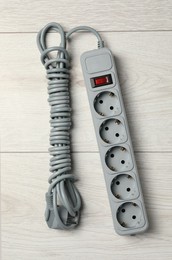 Photo of Power strip with extension cord on white wooden floor, top view. Electrician's equipment