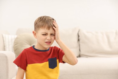 Photo of Little boy suffering from headache at home, space for text