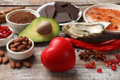 Photo of Natural aphrodisiac. Different food products and heart model on wooden table, closeup