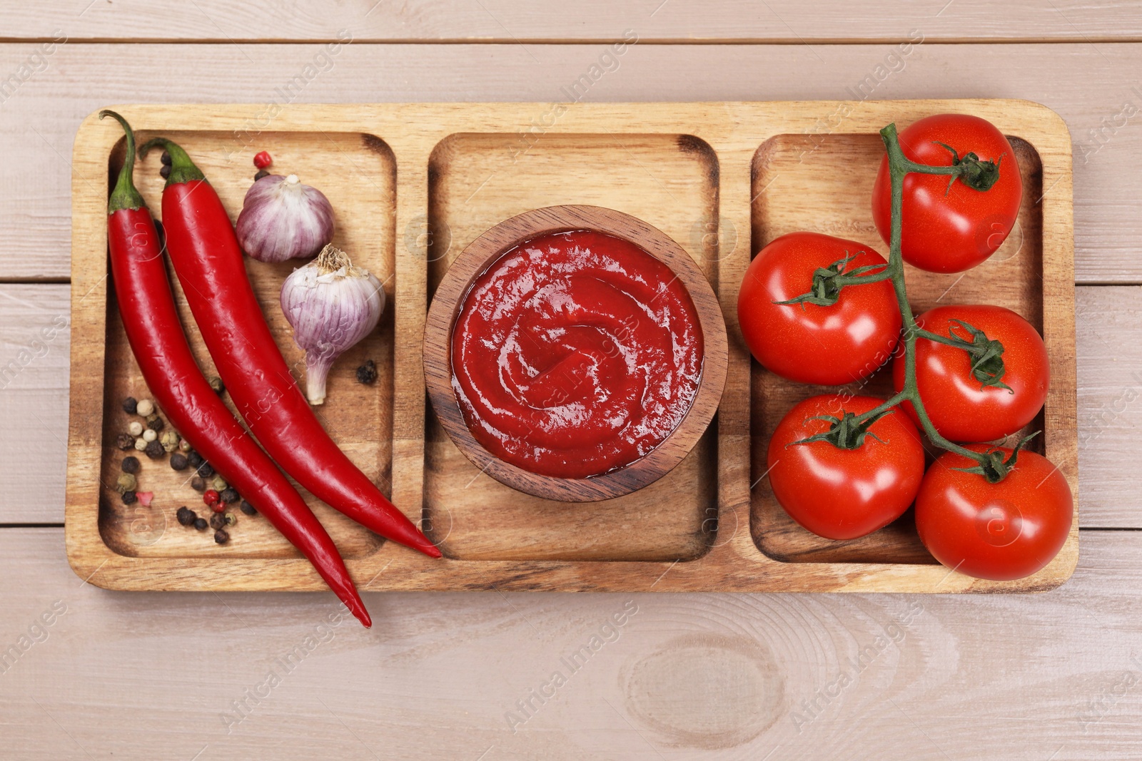 Photo of Plate with delicious ketchup in bowl, peppercorns and products on light wooden table, top view. Tomato sauce