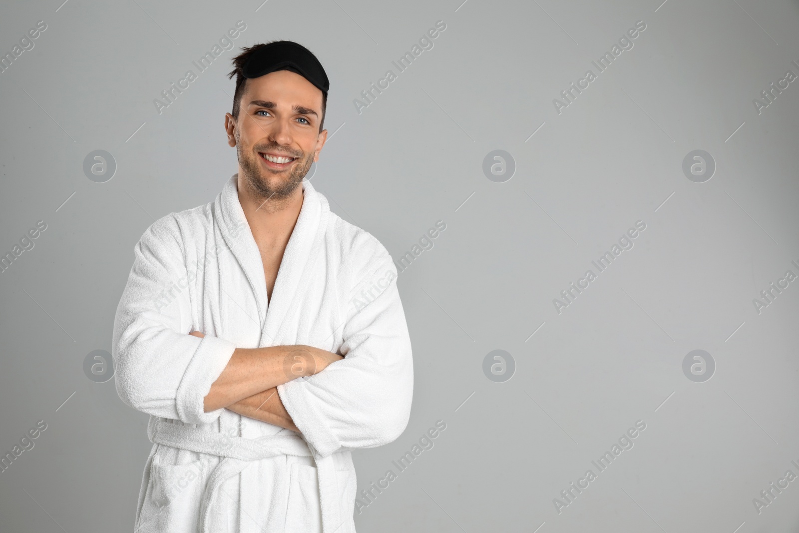 Photo of Happy young man in bathrobe on light grey background. Space for text