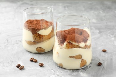 Photo of Delicious tiramisu in glasses and coffee beans on grey textured table, closeup