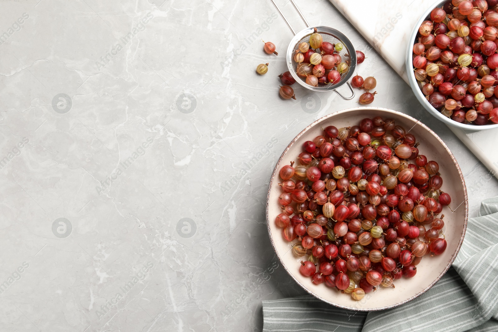 Photo of Ripe gooseberries on light grey marble table, flat lay. Space for text