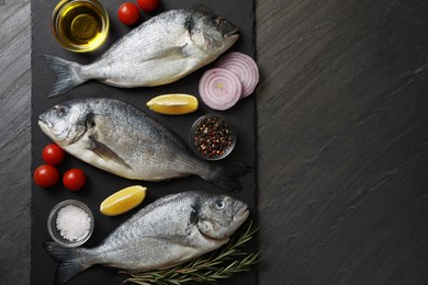 Photo of Fresh raw dorado fish, lemon, spices and tomatoes on black table, flat lay. Space for text