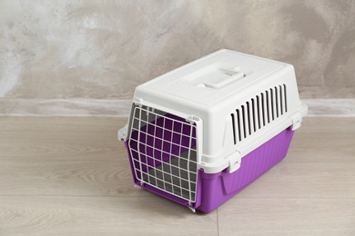 Photo of Violet pet carrier on floor near beige wall, space for text