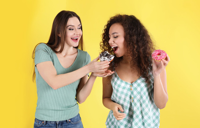 Beautiful young women with donuts on yellow background