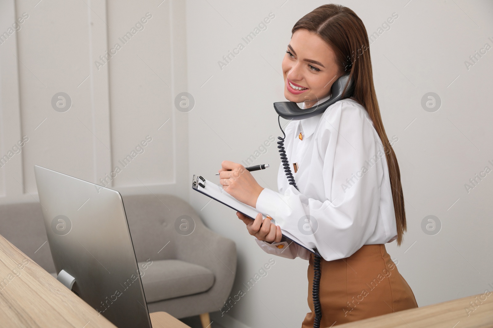 Photo of Female receptionist with clipboard talking on phone at workplace