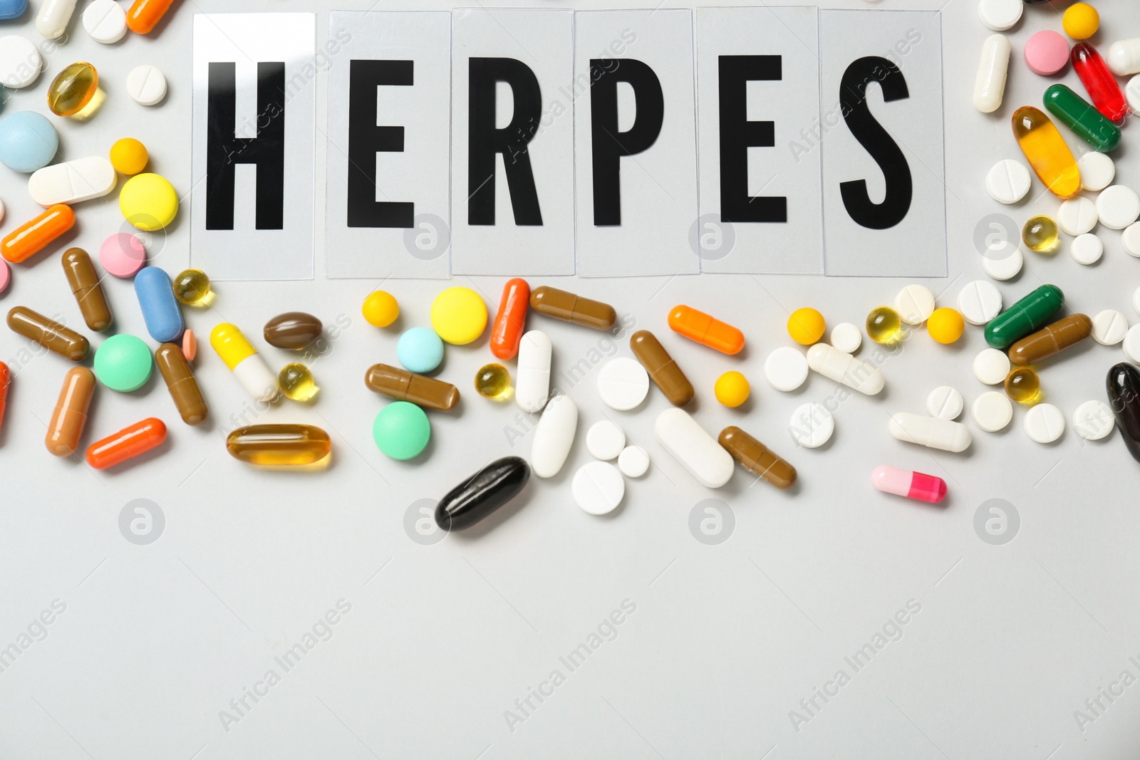 Photo of Word Herpes surrounded by different pills on white background, top view. Space for text