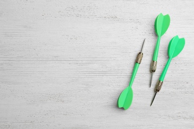 Photo of Green dart arrows on white wooden table, flat lay with space for text