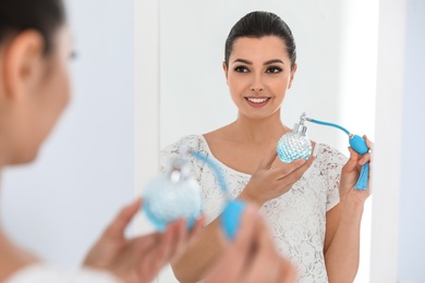 Photo of Young woman with bottle of perfume near mirror indoors