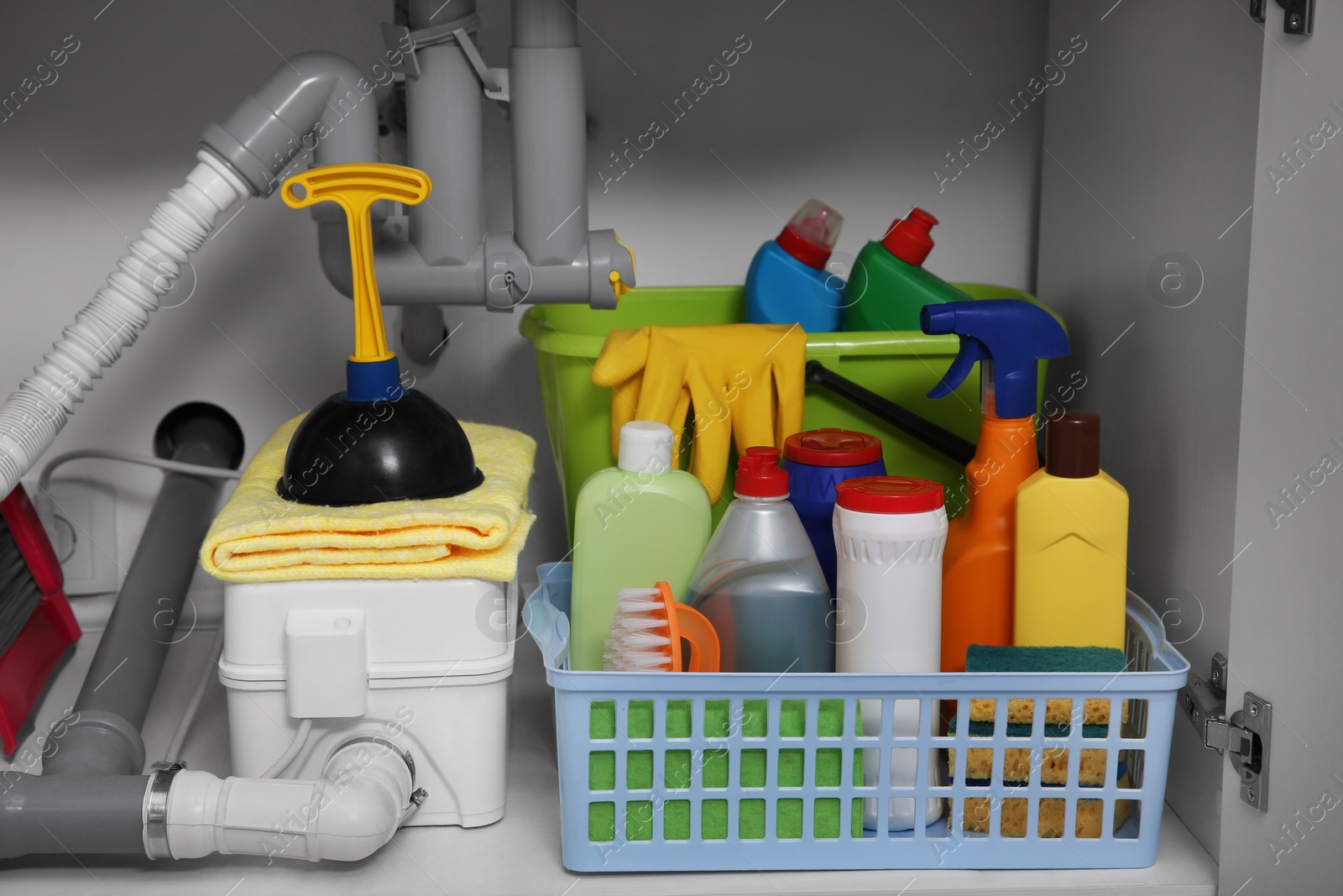 Photo of Open under sink cabinet with different cleaning supplies in kitchen