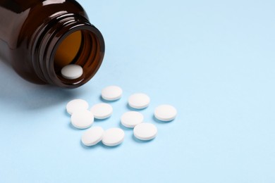 Photo of Plastic medical bottle with pills on light blue background, closeup. Space for text