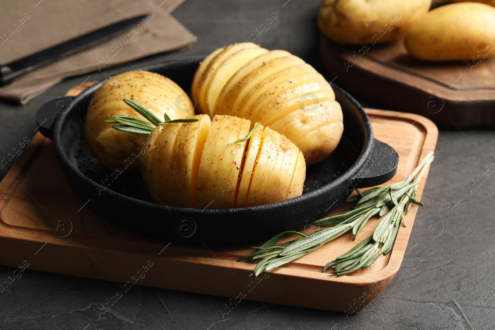 Photo of Raw Hasselback potatoes with rosemary in baking pan on dark grey table
