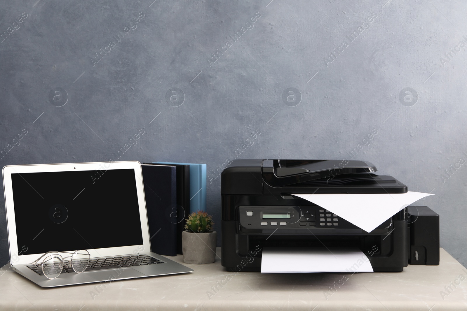 Photo of New modern printer and laptop on grey table at workplace