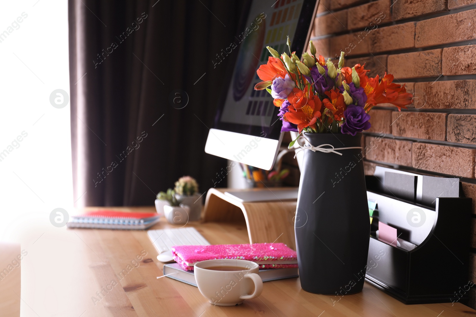 Photo of Stylish vase with fresh flowers and cup on wooden table at workplace