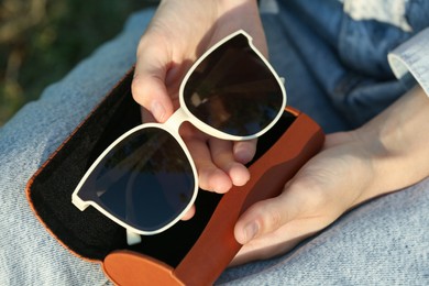Photo of Woman holding sunglasses in brown leather case outdoors on sunny day, above view