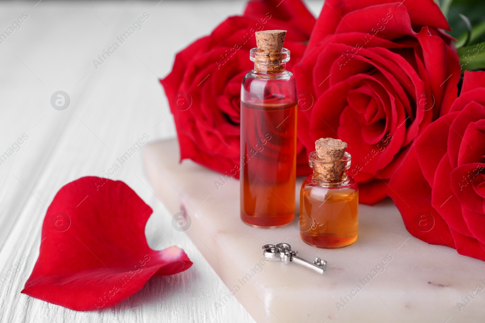 Photo of Bottles of love potion, red rose flowers and small key on white wooden table, closeup. Space for text