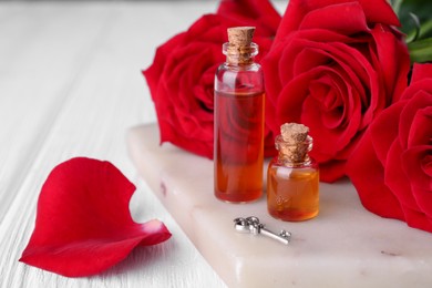 Photo of Bottleslove potion, red rose flowers and small key on white wooden table, closeup. Space for text