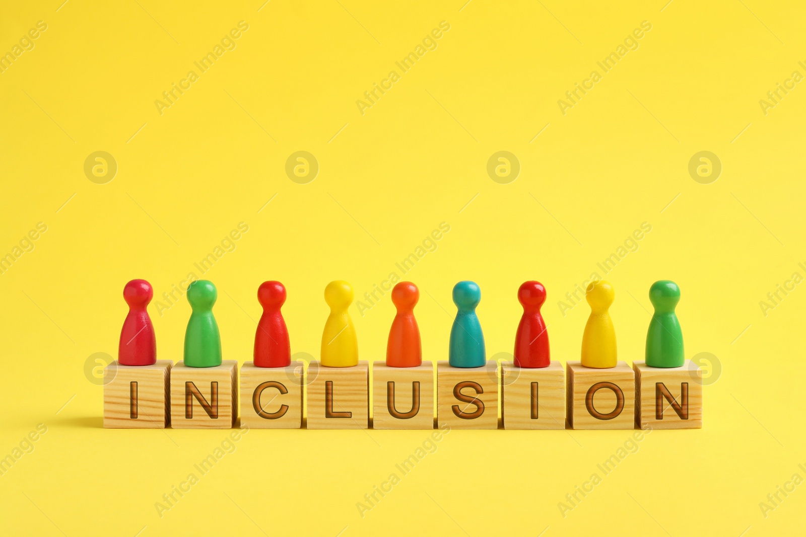 Photo of Colorful pawns and cubes with word Inclusion on yellow background