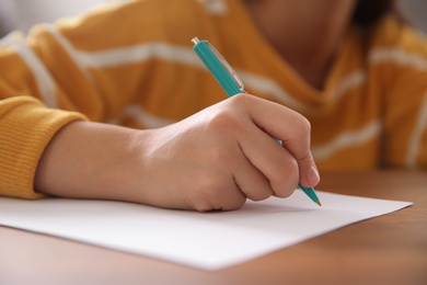 Photo of Woman writing letter at wooden table indoors, closeup