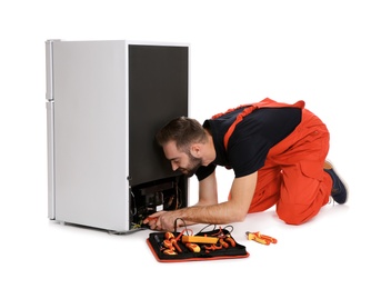 Male technician in uniform repairing refrigerator on white background