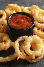 Photo of Delicious golden crispy onion rings and sauce on gray background, closeup