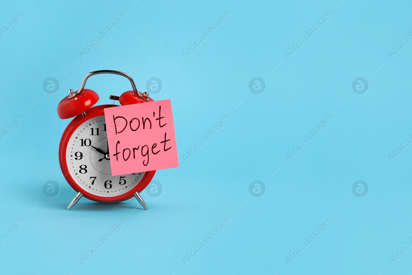 Photo of Alarm clock and reminder note with phrase Don't forget on light blue background, space for text