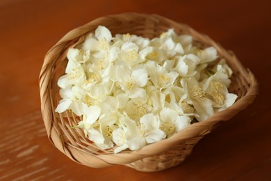 Photo of Beautiful white jasmine flowers in wicker basket on wooden table, closeup